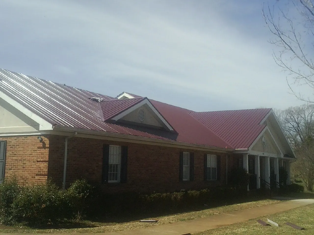 Red metal roof with gabled entries on a long brick building, from a Hail Damage Roof Repair job in Clearwater Beach