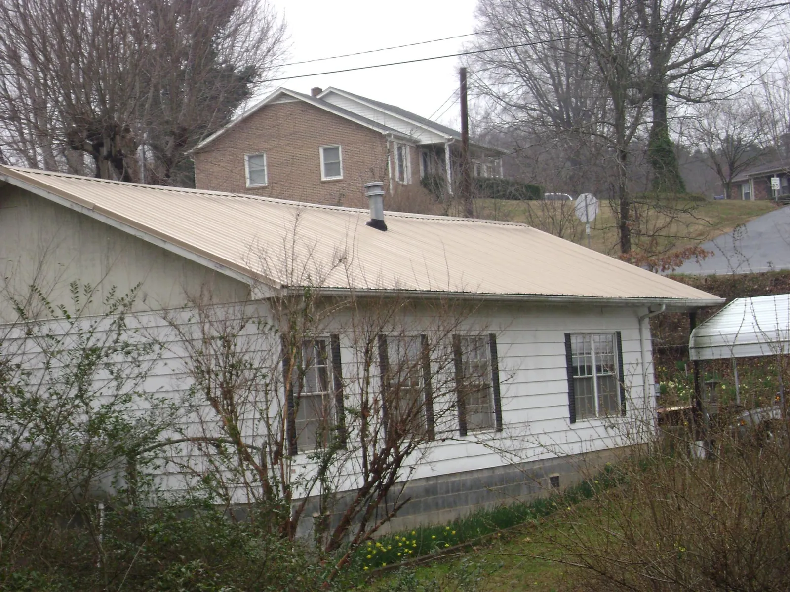 Tan metal roof on a white sided house set into a hillside — Commercial Roofing by Roofing Brothers in Clearwater Beach